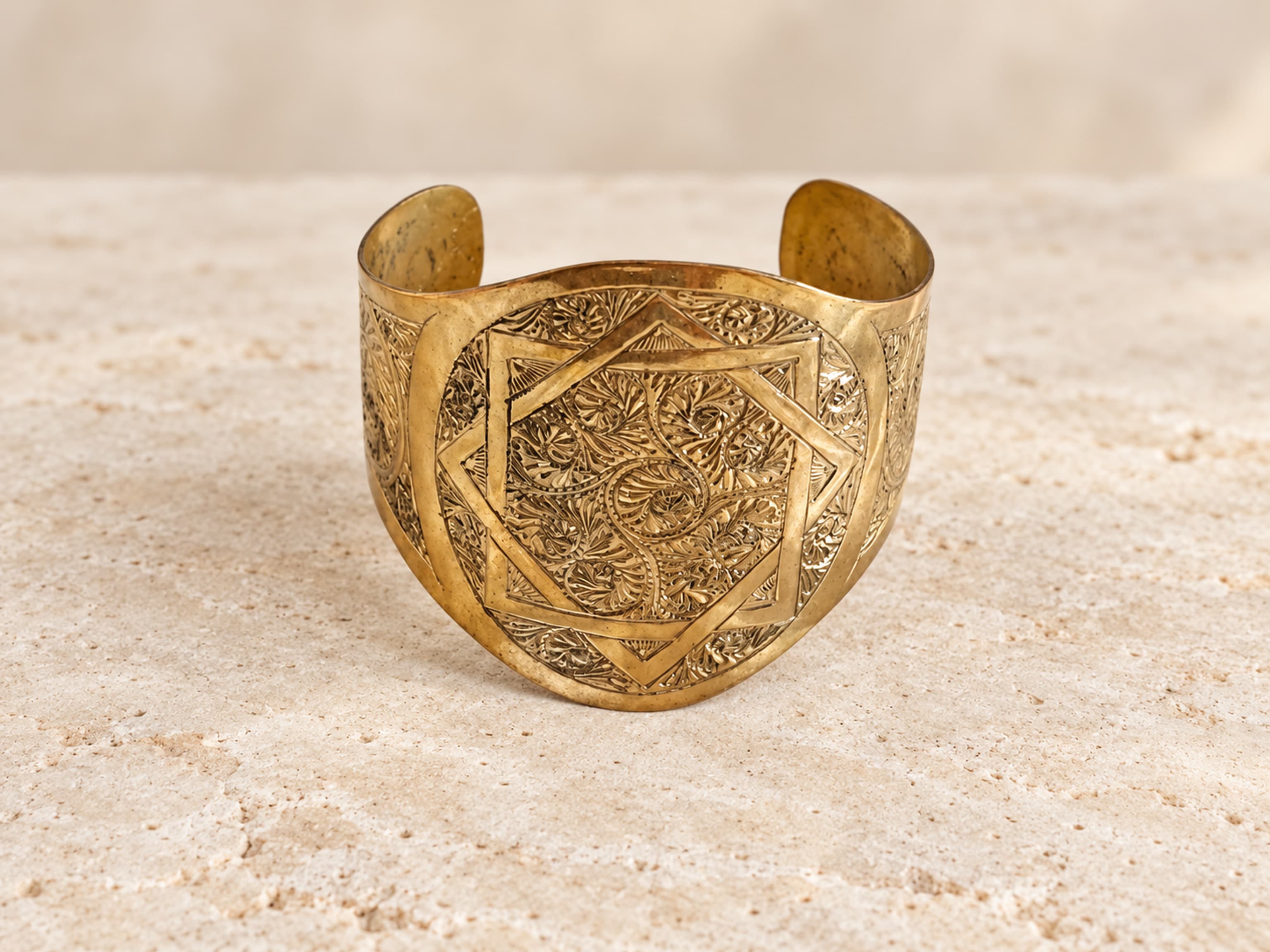 Vista frontal del brazalete abierto de latón con estrella geométrica y motivos vegetales grabados.