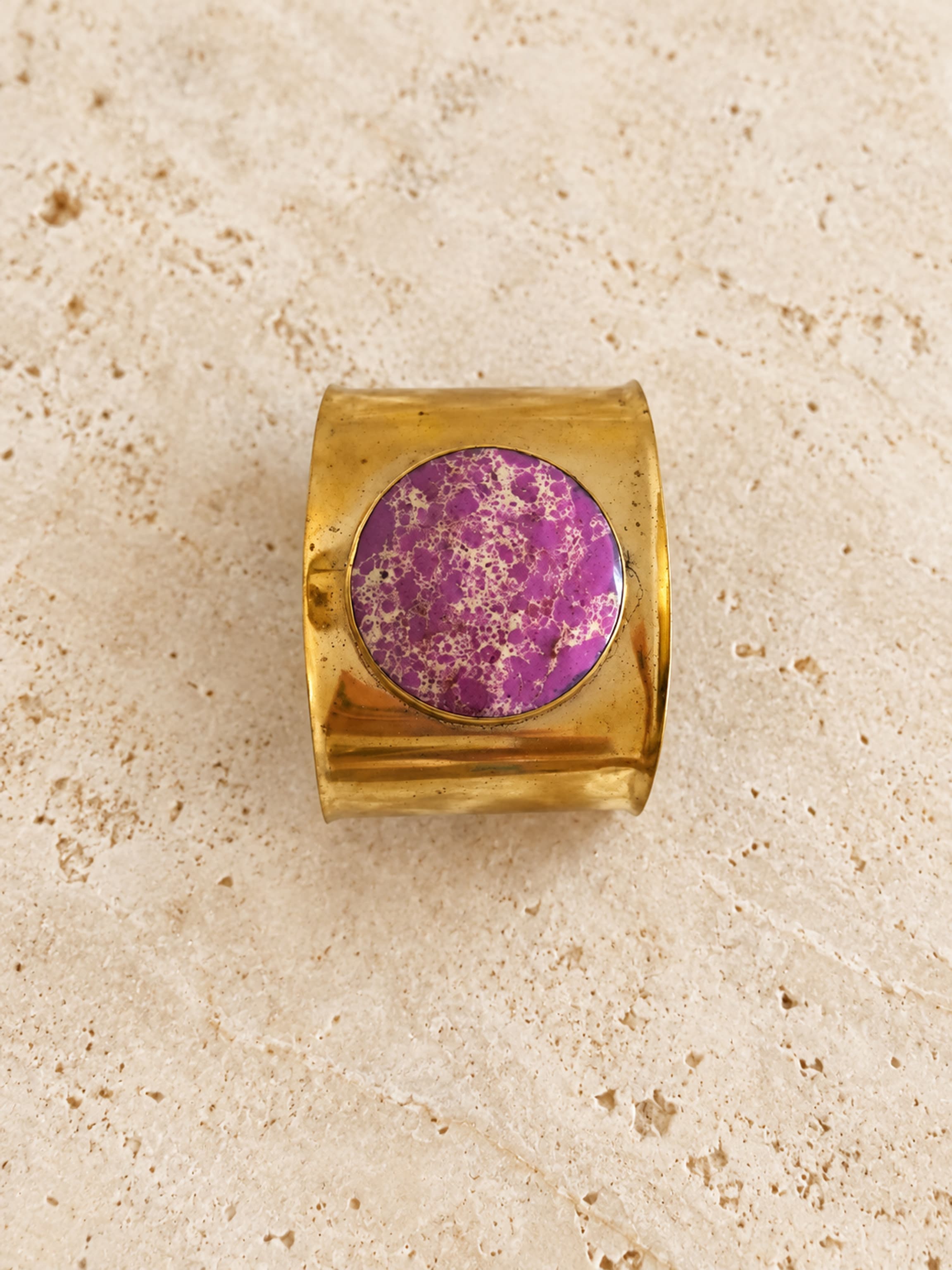 Vista del brazalete ancho de latón dorado con piedra lila redonda y vetas color crema.